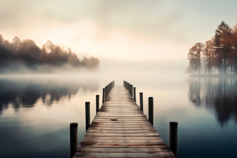 Hölzerner Steg, der in einen morgendlich nebligen See führt